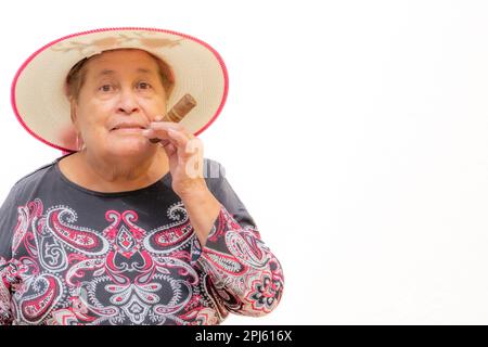 Sorpresa vecchia donna che fuma un sigaro su sfondo bianco, guardando la macchina fotografica, espressione maliziosa, nonna che indossa un cappello in una giornata di sole. Con Foto Stock