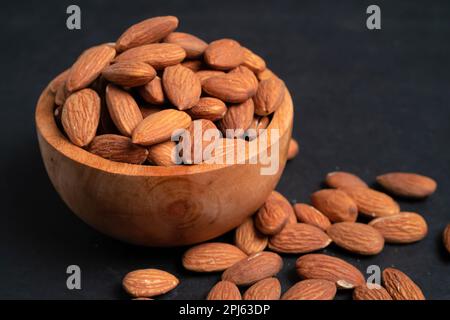 Mandorle pelate in una ciotola di legno e alcune noci sparse su fondo nero Foto Stock