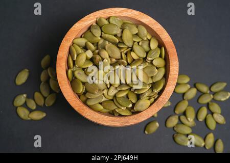 Semi di zucca in una ciotola di legno su sfondo scuro Foto Stock
