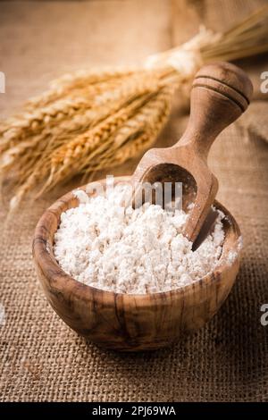 Farina in recipiente di legno con grano su fondo di tela Foto Stock