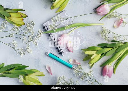 Area di lavoro con diario, notebook, penna, fiori su sfondo azzurro. Scrivania da ufficio domestico. Vista dall'alto sfondo femminile. Piano di giacitura, vista dall'alto Foto Stock