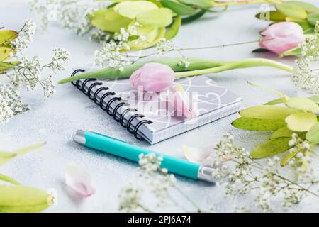 Area di lavoro con diario, notebook, penna, fiori su sfondo azzurro. Scrivania da ufficio domestico. Vista dall'alto sfondo femminile. Piano di giacitura, vista dall'alto Foto Stock