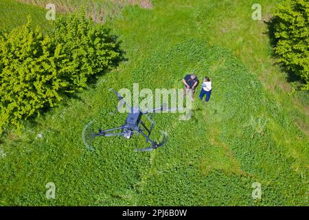 Squadra di soccorso che gestisce il drone che sorvola il prato per individuare i caprioli nascosti nell'erba con termocamera prima di tagliare i prati in primavera Foto Stock