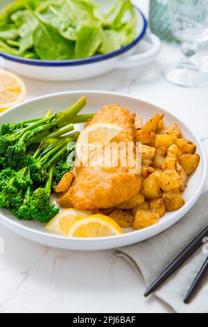 Filetto di fisch impanato con patate piccanti al forno e insalata di broccoli (bimi) con limone Foto Stock