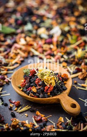 Foglie di tè essiccato, frutta e bacche in ciotola su tavola rustica di legno Foto Stock