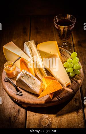 Piatto di formaggi, assortimento di formaggi diversi con bicchiere di vino rosso, uva su tavola di legno Foto Stock