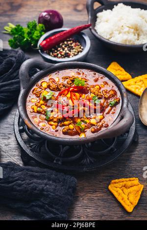 Ciotola di peperoncino con carne con riso e condimenti su tavola di legno Foto Stock