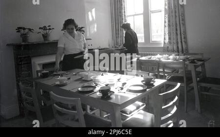 1950s, storico, le donne membri del personale di cucina che posano i tavoli nella sala da pranzo presso l'ostello a Littlemore, una struttura di salute mentale presso il Littlemore Hospital, Oxfordshire, Inghilterra, Regno Unito. Foto Stock