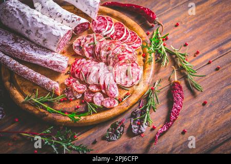 Salumi - assortimento di salumi e salsicce essiccati all'aria su tagliere di legno con spezie Foto Stock