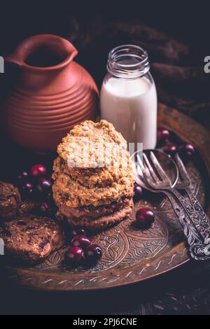 Biscotti fatti in casa con farinata d'avena, biscotti al mirtillo e una bottiglia di latte su un tavolo di legno Foto Stock