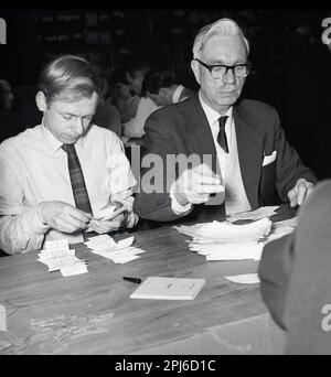 1960s, storico, due maschi, uno anziano, l'altro giovane, Seduta che conta i voti a mano nella circoscrizione di St Pancras North alle elezioni generali del 1964, Londra, Inghilterra, Regno Unito. St Pancras North è stato creato nel 1885 ed eletto membro del Parlamento fino al 1983, quando la zona è diventata parte di una nuova circoscrizione, Holborn e St Pancras. Foto Stock