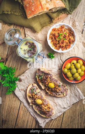 Patata fresca fatta in casa di fegato di pollo su pane ciabatta con cipolle arrostite e olive su tavola di legno Foto Stock