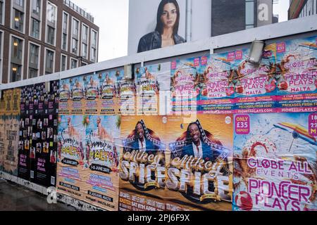 Street scene a Whitechapel, dove una guardia intorno a un cantiere edile è coperta da poster pubblicitari per varie serate di club il 8th marzo 2023 a Londra, Regno Unito. Foto Stock