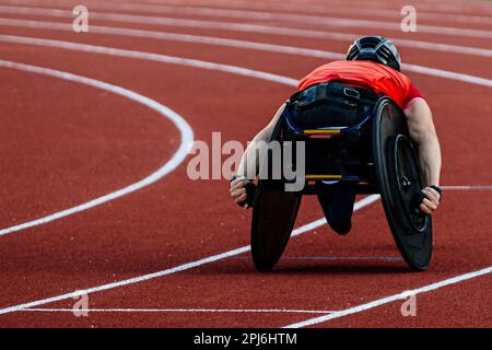 atleta maschile in sedia a rotelle corsa pista rossa stadio in gara di atletica para, giochi sportivi estivi Foto Stock