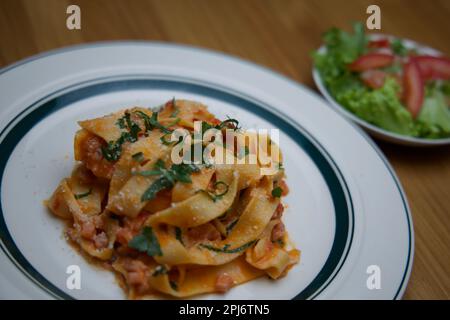 Un delizioso piatto di pasta italiana esposto su un piatto bianco con insalata sullo sfondo Foto Stock
