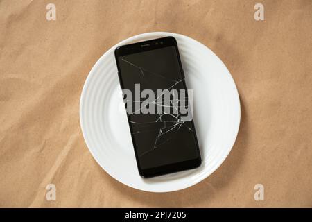 telefono nero con schermo incrinato su una piastra bianca Foto Stock