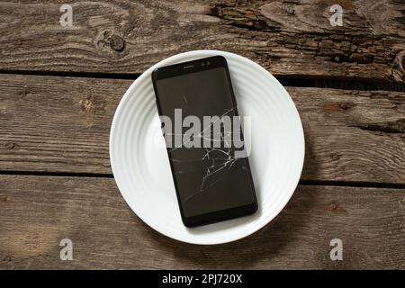 telefono nero con schermo incrinato su una piastra bianca Foto Stock