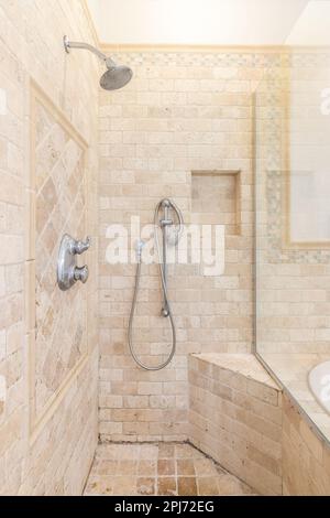 Una cabina doccia con piastrelle di pietra quadrata marrone, una piccola panca incorporata e rubinetti cromati. Foto Stock