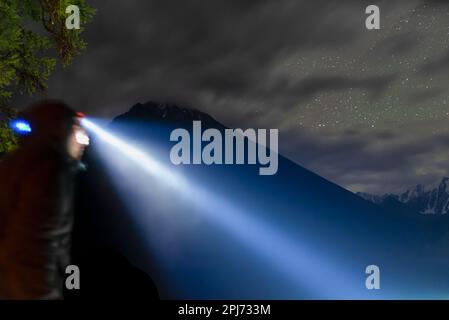 Foto astratta di un fascio di una lampada frontale su una ragazza turistica nel buio delle montagne sotto il cielo stellato di notte. Foto Stock
