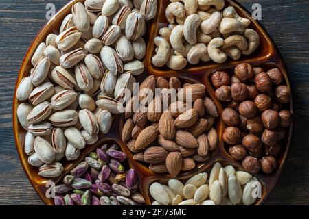 Assortimento di noci in ceramica su fondo legno, primo piano, vista dall'alto, spazio copia. Anacardi, nocciole, pistacchi e mandorle noci da mangiare. Veg Foto Stock