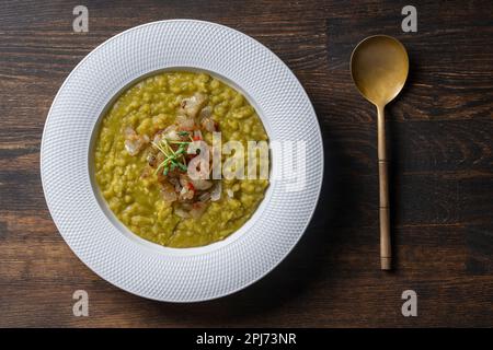 Purea di piselli verdi con cipolle fritte in un piatto bianco con spezie sul tavolo, primo piano, vista dall'alto. Cibo sano, deliziosa zuppa di piselli secchi Foto Stock