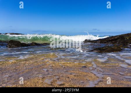 Vista dall'angolo basso dell'onda che si getta sulla spiaggia con cielo azzurro sopra Foto Stock
