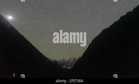 Stella polare brillante su una montagna con ghiacciai di notte con la luce di un camper turistico sulla riva di un lago in Altai in Russia. Foto Stock