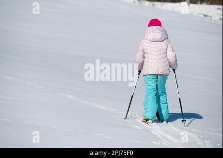 Vista posteriore di una giovane ragazza che attraversa una neve fresca con gli sci di fondo. Foto Stock