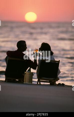 Una coppia afroamericana brinda l'un l'altro con un bicchiere di vino ben guardando il tramonto su una spiaggia del North Carolina Foto Stock