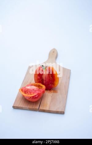 una foto verticale un pomodoro di cimelio tagliato a metà su un tagliere di legno con uno sfondo bianco Foto Stock