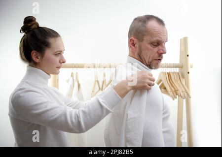 Personalizzare in piedi vicino al cliente maschio che misura la schiena. Personalizzare la donna prendendo misure per la camicia di lavoro con metro a nastro. Giovane stilista di moda che misura l'uomo che indossa la camicia in negozio Foto Stock