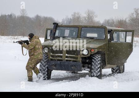 KRASNOYE SELO, RUSSIA - 19 FEBBRAIO 2023: Un camuffatore con un fucile d'assalto Kalashnikov si posiziona sulla Tiger blindata su neve Foto Stock