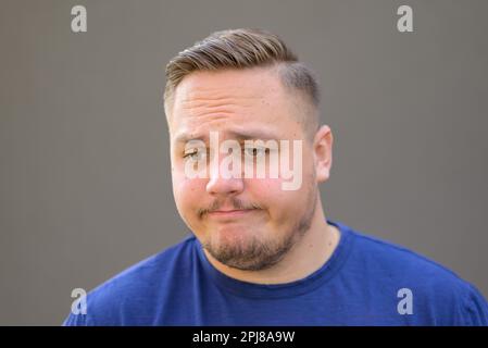 Giovane uomo con uno sguardo triste e premuroso verso il basso su uno sfondo grigio Foto Stock