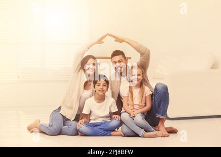 Famiglia felice che forma il tetto della casa con le loro mani a casa. Concetto di assicurazione Foto Stock