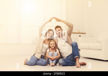 Famiglia felice che forma il tetto della casa con le loro mani a casa. Concetto di assicurazione Foto Stock