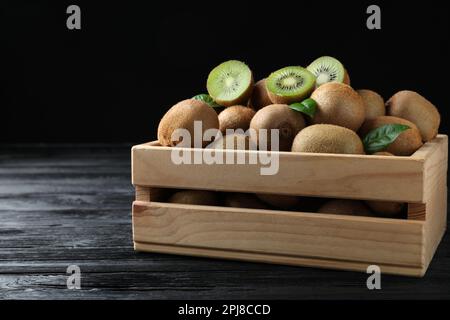 Cassa con kiwi tagliati e interi freschi su tavolo di legno nero Foto Stock