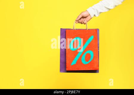 Uomo che tiene la borsa di shopping di carta con segno di percentuale su sfondo giallo, primo piano. Concetto di sconto Foto Stock