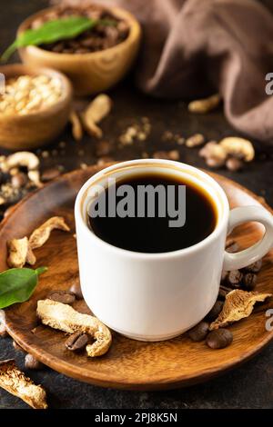 Sano organico energizzante adattogeno. Caffè ai funghi in una tazza e caffè in grani, bevanda alla moda su uno sfondo di pietra. Foto Stock