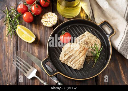 Ristorante cibo. Frutti di mare. Stile rustico. Succosa bistecca di tonno cucinata con spezie, pomodori e rosmarino su un piatto di pietra. Foto Stock