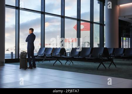 Uomo d'affari con valigia e borsa nell'area d'attesa dell'aeroporto Foto Stock