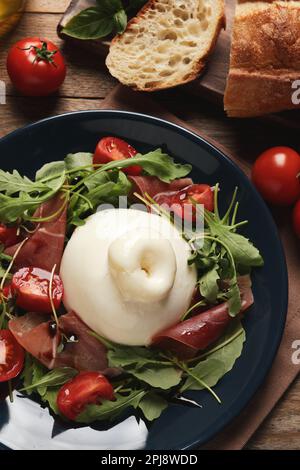 Deliziosa insalata di burrata con pomodori, prosciutto e rucola su tavolo di legno, piatto Foto Stock