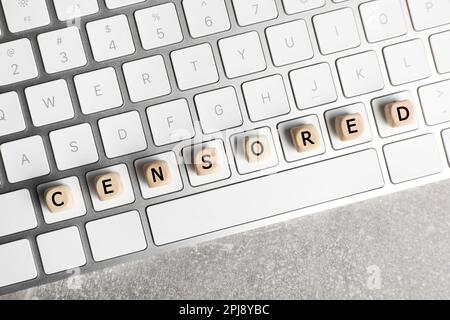 Cubi di legno con parola censurata e tastiera su tavolo grigio chiaro, vista dall'alto Foto Stock