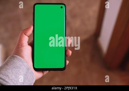 Mano donna che mostra lo schermo verde dello smartphone. Schermo del telefono con chiave chroma in posizione verticale. Foto mockup con spazio di copia. Internet delle cose. Foto Stock