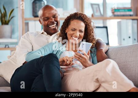 Coppia, telefono e ridere sul divano nel salotto di casa, commedia sui social media e divertirsi. Interracial, cellulare e divertente uomo nero e maturo Foto Stock
