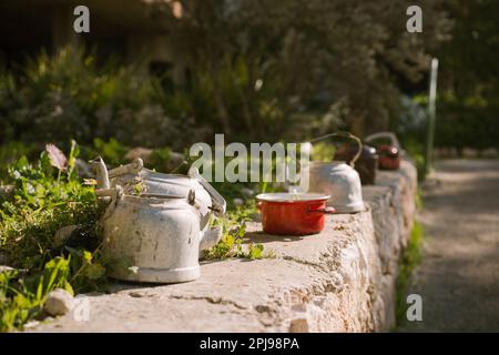 Teiere vintage e pot in Garden Design il giorno del sole. Luce del sole brillante evidenzia la tessitura rustica e intemperiata delle teiere e delle Pot, migliorando l'atmosfera vintage del decor sostenibile del Giardino Foto Stock