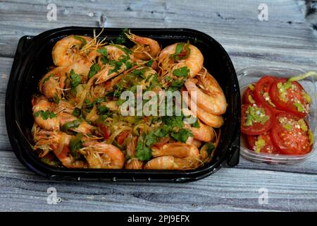 Gamberetti bolliti con aglio, limone, prezzemolo, pepe, cipolla e pomodoro, fette sottaceto di pomodori e peperoni verdi servite in pl nero usa e getta Foto Stock