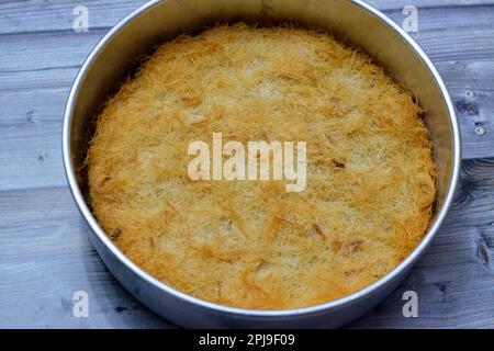 Un tradizionale dessert mediorientale Knafeh Konafa fatto con kataifi di pasta filata, imbevuto in uno sciroppo di miele di zucchero dolce, stratificato con formaggio, o coagulato Foto Stock