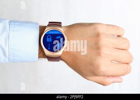 Giovane uomo che mostra orologio da polso elettronico con interfaccia Smart Home su sfondo chiaro, primo piano Foto Stock