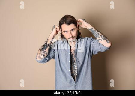 Giovane uomo con tatuaggi sul corpo su sfondo beige Foto Stock
