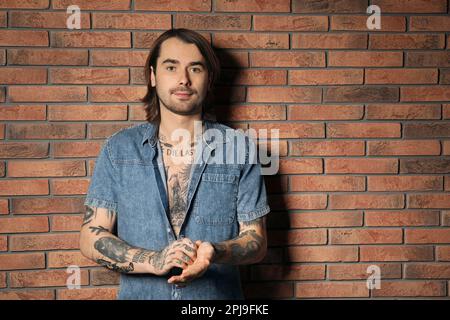 Giovane uomo con tatuaggi sul corpo vicino al muro di mattoni Foto Stock